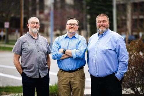 Three business men standing side by side and smiling at the camera